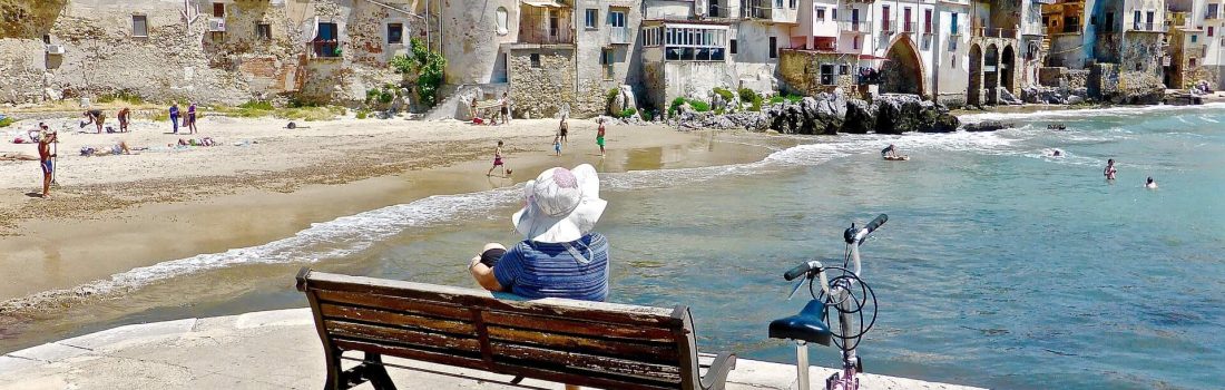 Person sitting on bench overlooking Cefalu beach
